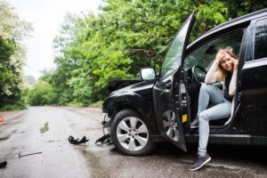 young woman in the damaged car after a car accident, making a phone call