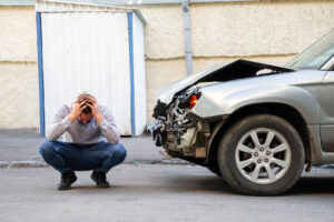 Young man driver in car accident holding his head near broken car on the road after car accident